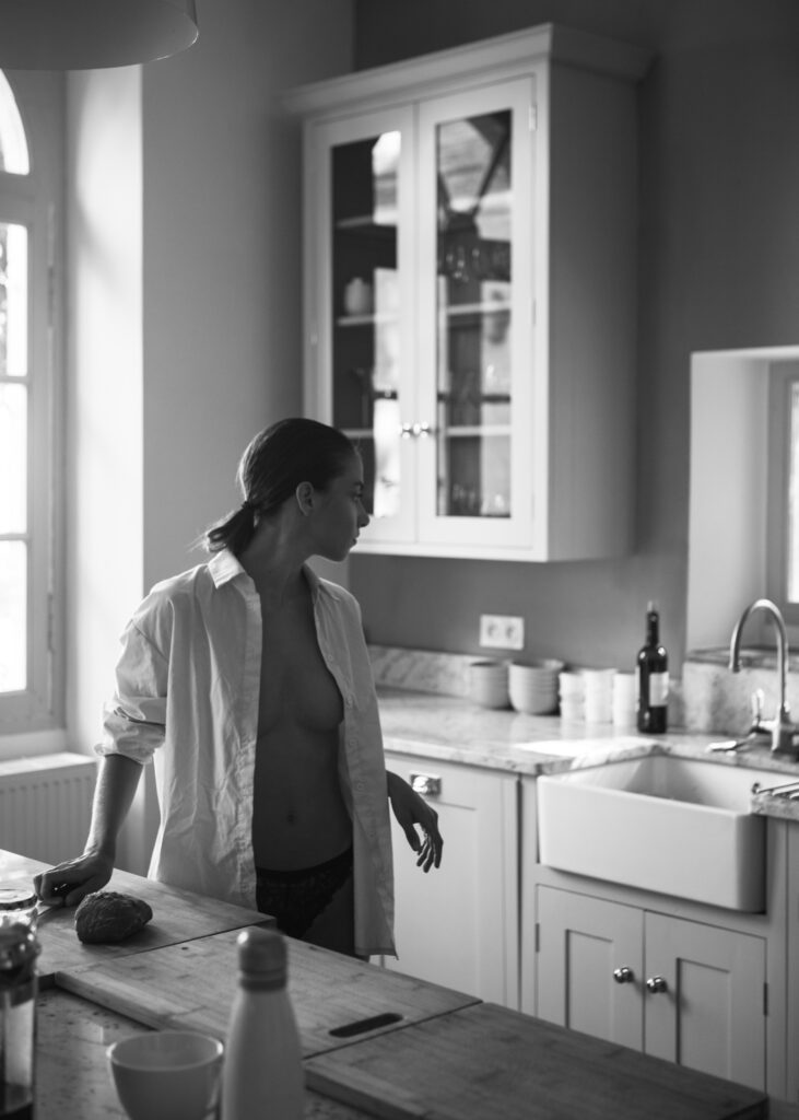 Rebecca Bagnol in "Breakfast with Rebecca" — nude series by Hannes Walendy, 2024. Rebecca in the kitchen, shirt open, nipples visible, shot in black and white.